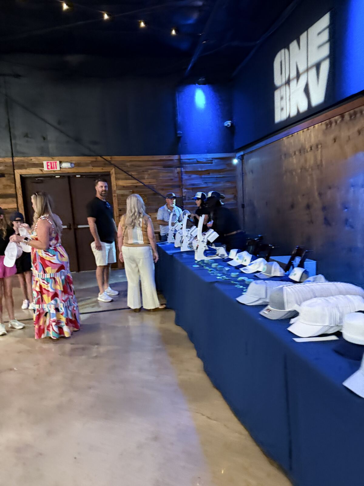Diverse crowd at a night event wearing decorated t-shirts beneath a branded display booth