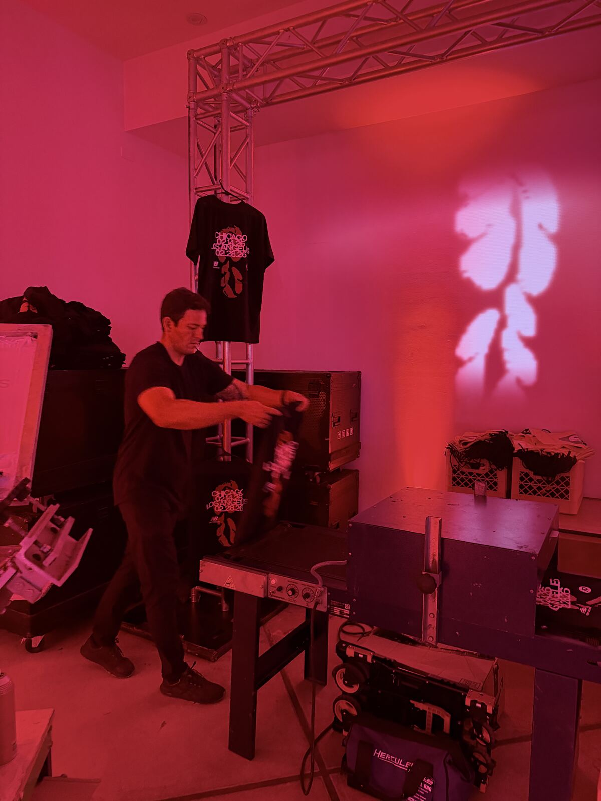 Wide view of a trade show booth with displayed t-shirts, printing equipment, and multiple attendees